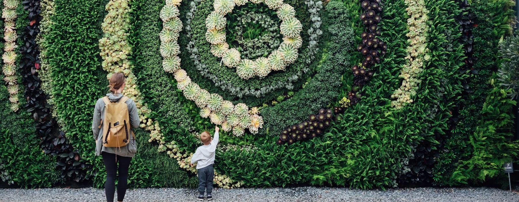 mother and child standing in front of a mural made of plants